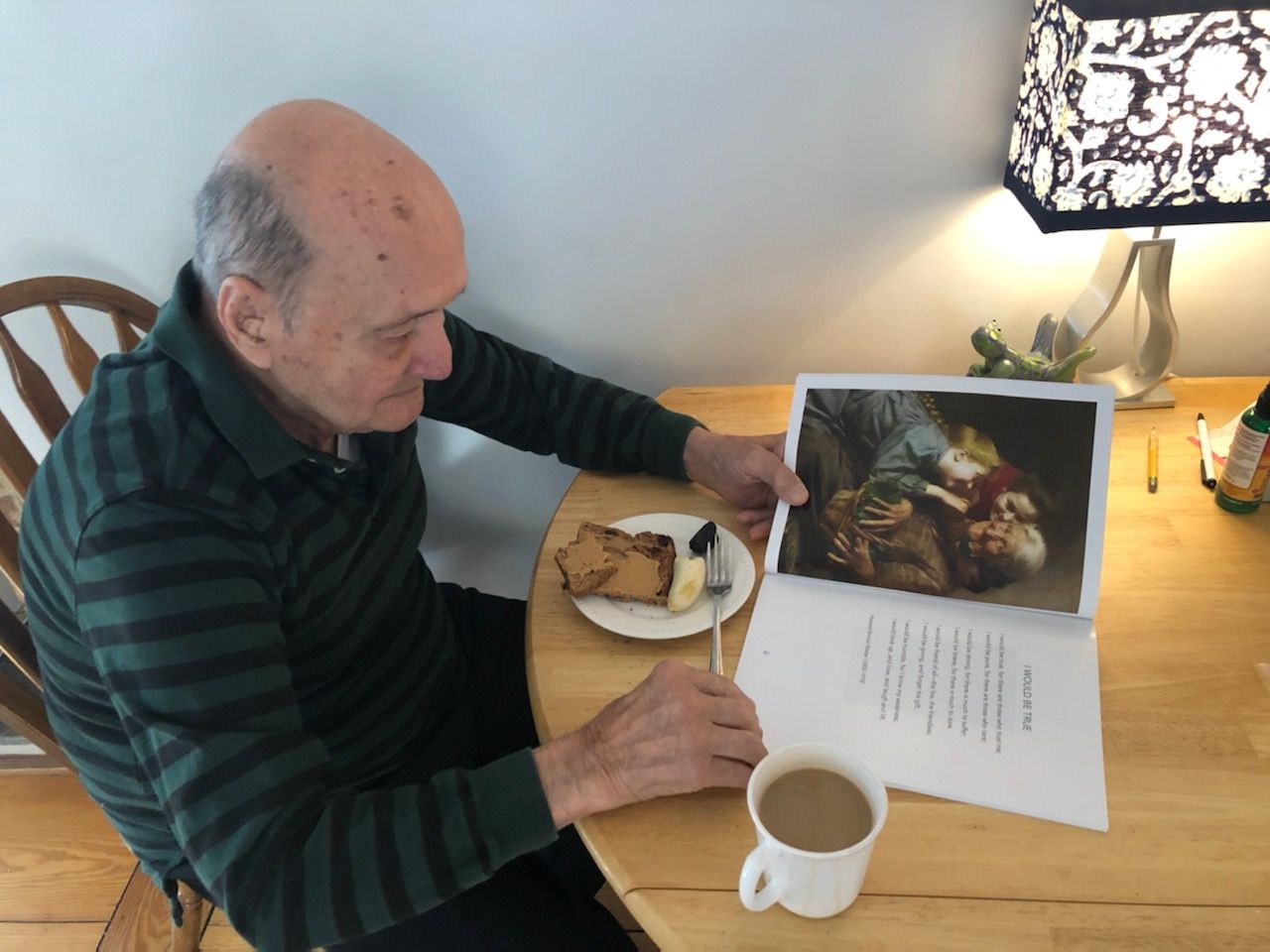 Elderly veteran living with dementia sits with his coffee and breakfast as he reads a nostalgic picture book. NANA’S BOOKS are a joy for people of all ages.