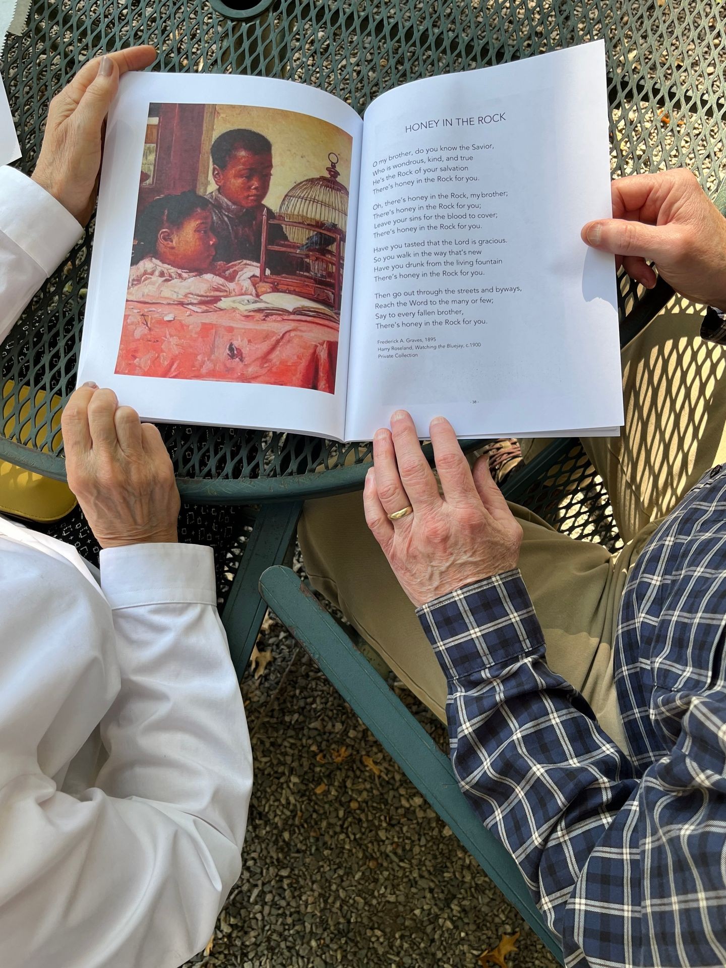 Two older adults sharing a bespoke book for Alzheimer’s and dementia care. A man and a woman’s hands are shown, as they share a traditional Gospel poem, ‘Honey in the Rock.’ 